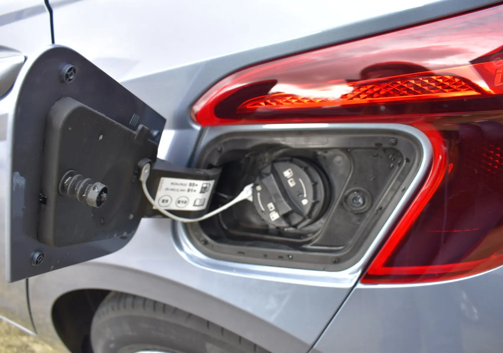 Gros plan sur l'ouverture de la trappe à carburant côté gauche d'une Hyundai i20 bleu clair avec feu arrière rouge.