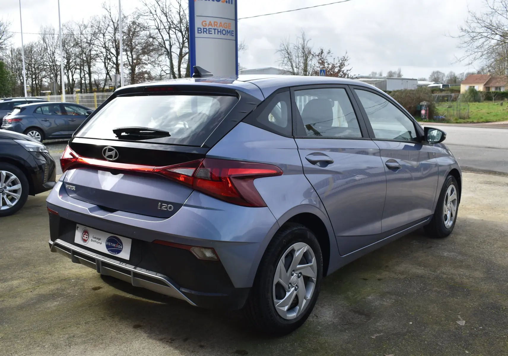 Vue 3/4 arrière droite d'une Hyundai i20 bleu clair 2025 avec spoiler de toit et feux arrière distinctifs en forme de flèche.