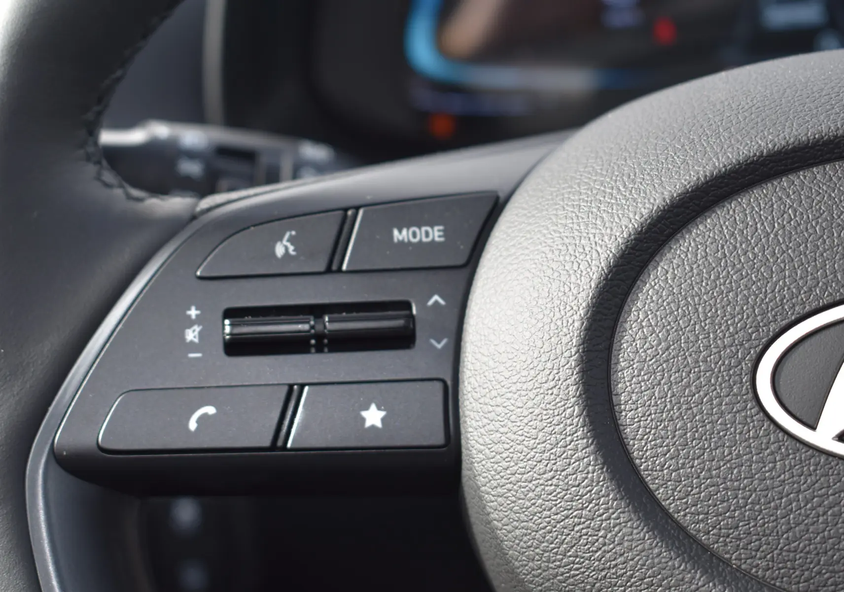 Gros plan sur les commandes audio au volant d'une Hyundai i20 2025, volant en cuir gris foncé.