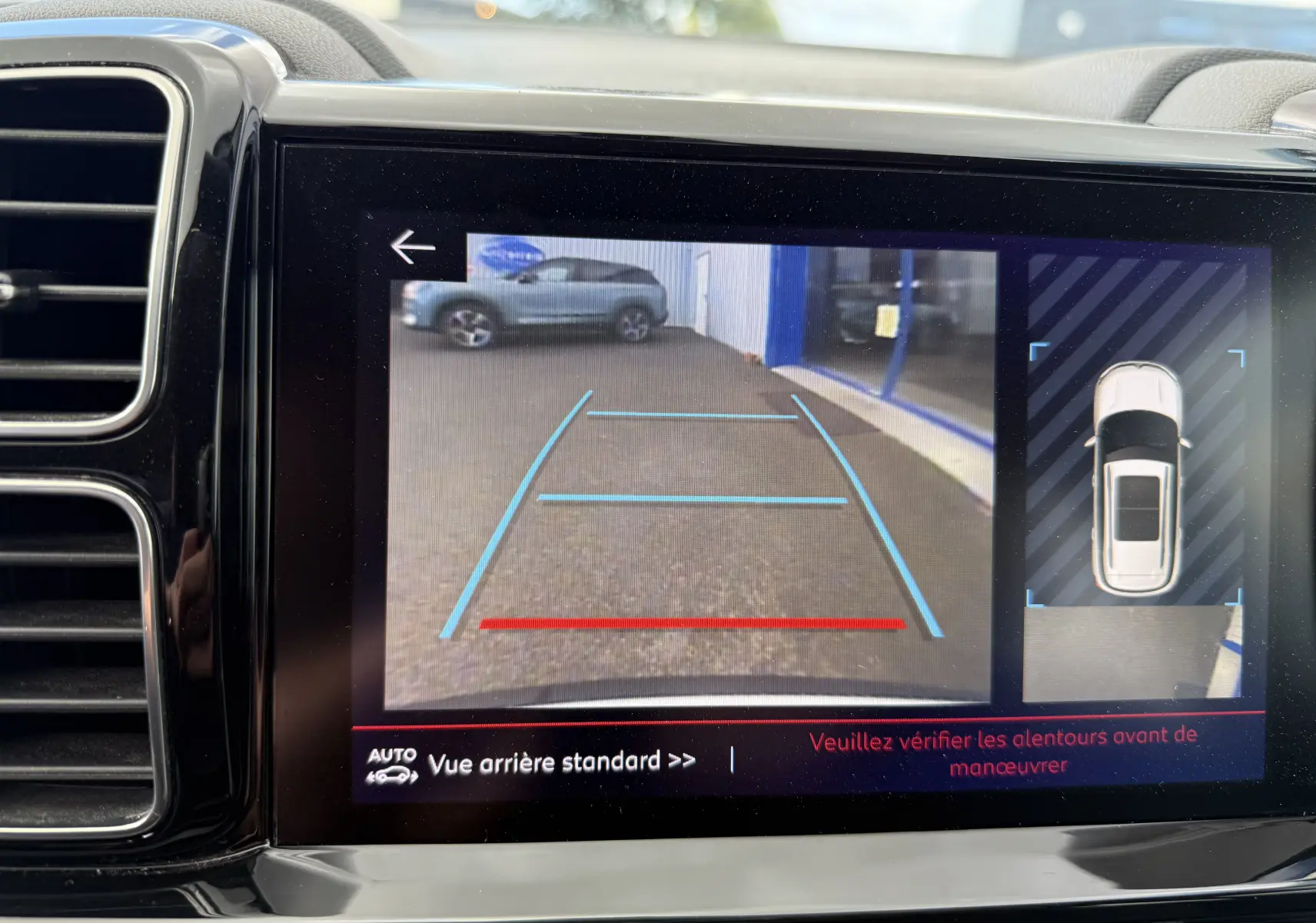 Écran de caméra de recul montrant une Citroën C5 Aircross blanche vue de dessus et arrière en stationnement.