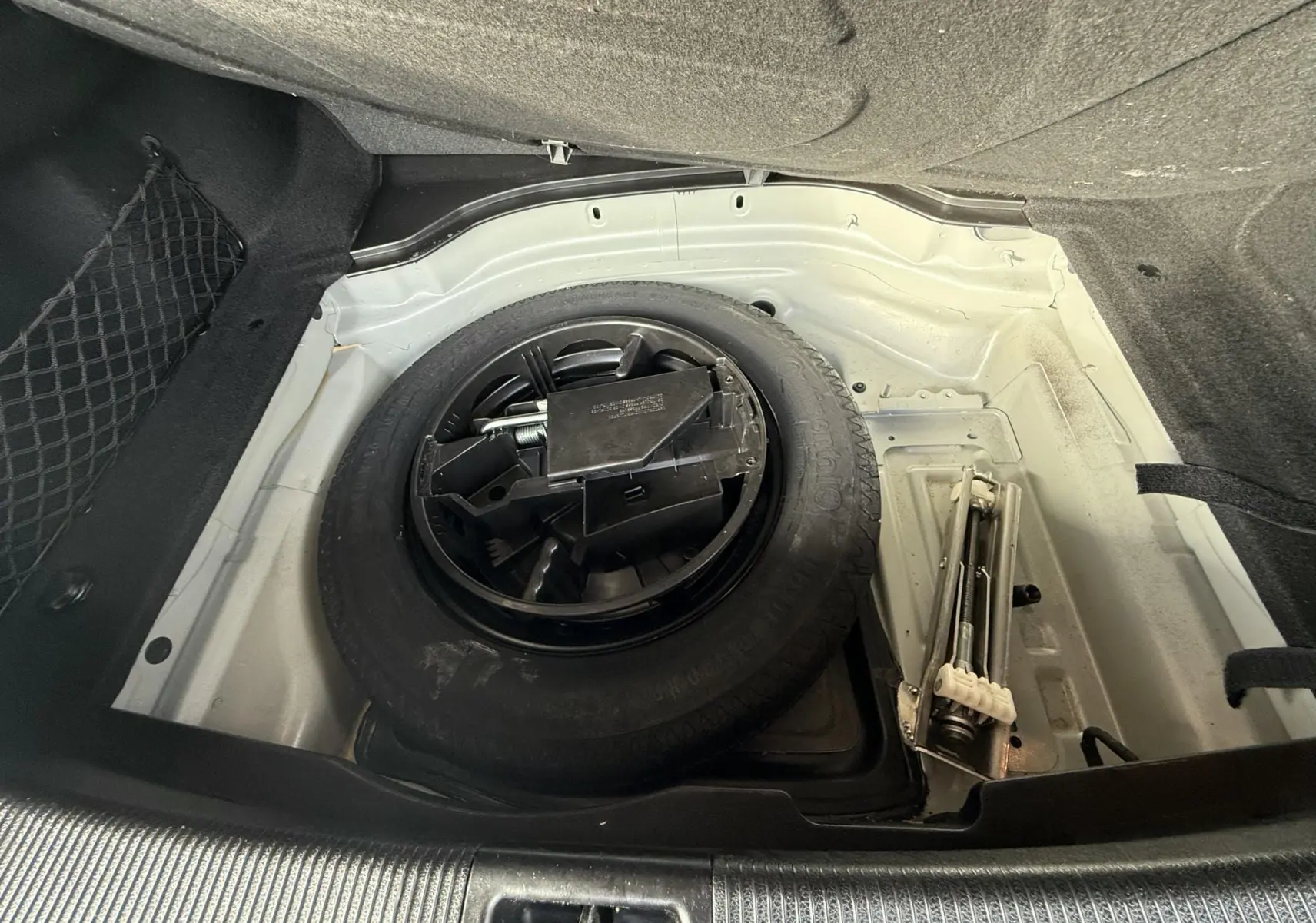 Vue plongeante sur la roue de secours et le cric dans le coffre d'une Mercedes Classe E 250 Coupé gris.