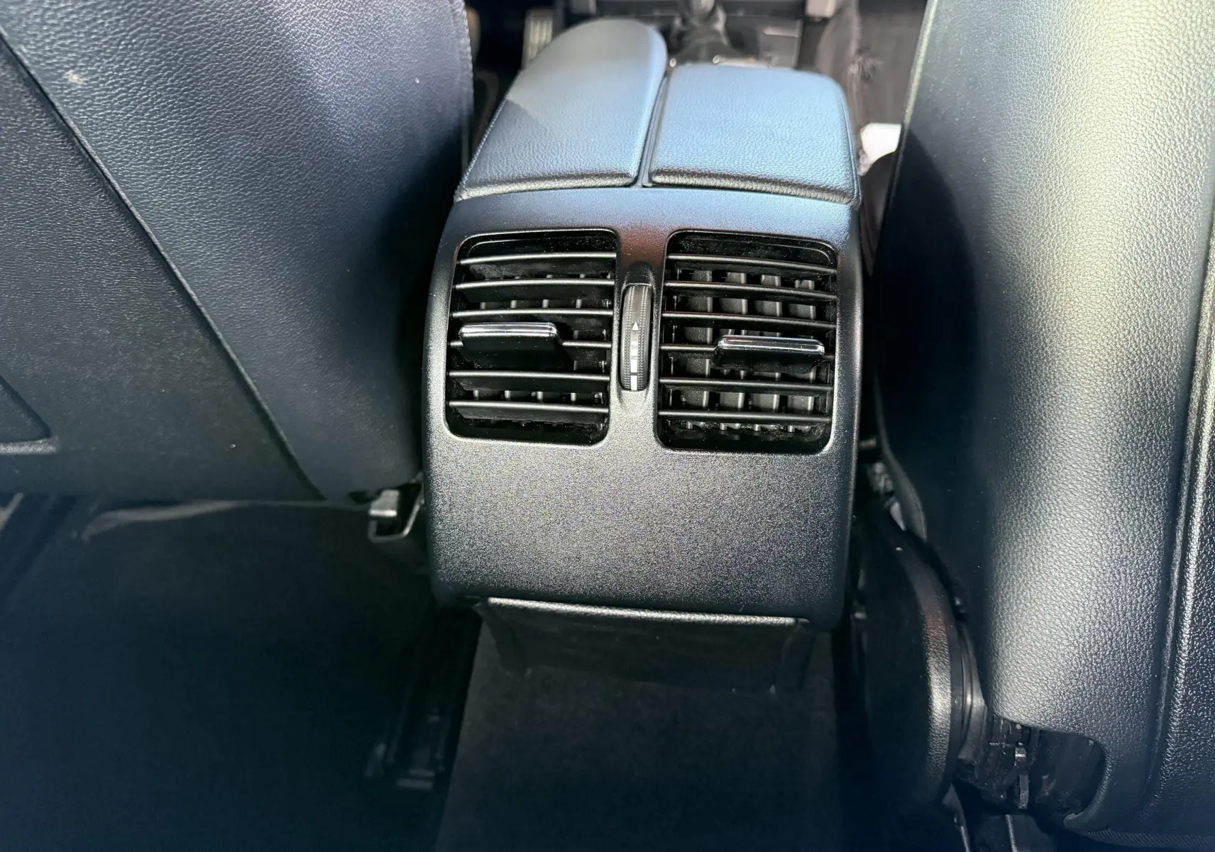 Gros plan sur les aérateurs arrière noirs entre les sièges avant d'une Mercedes Classe E 250 Coupé gris.