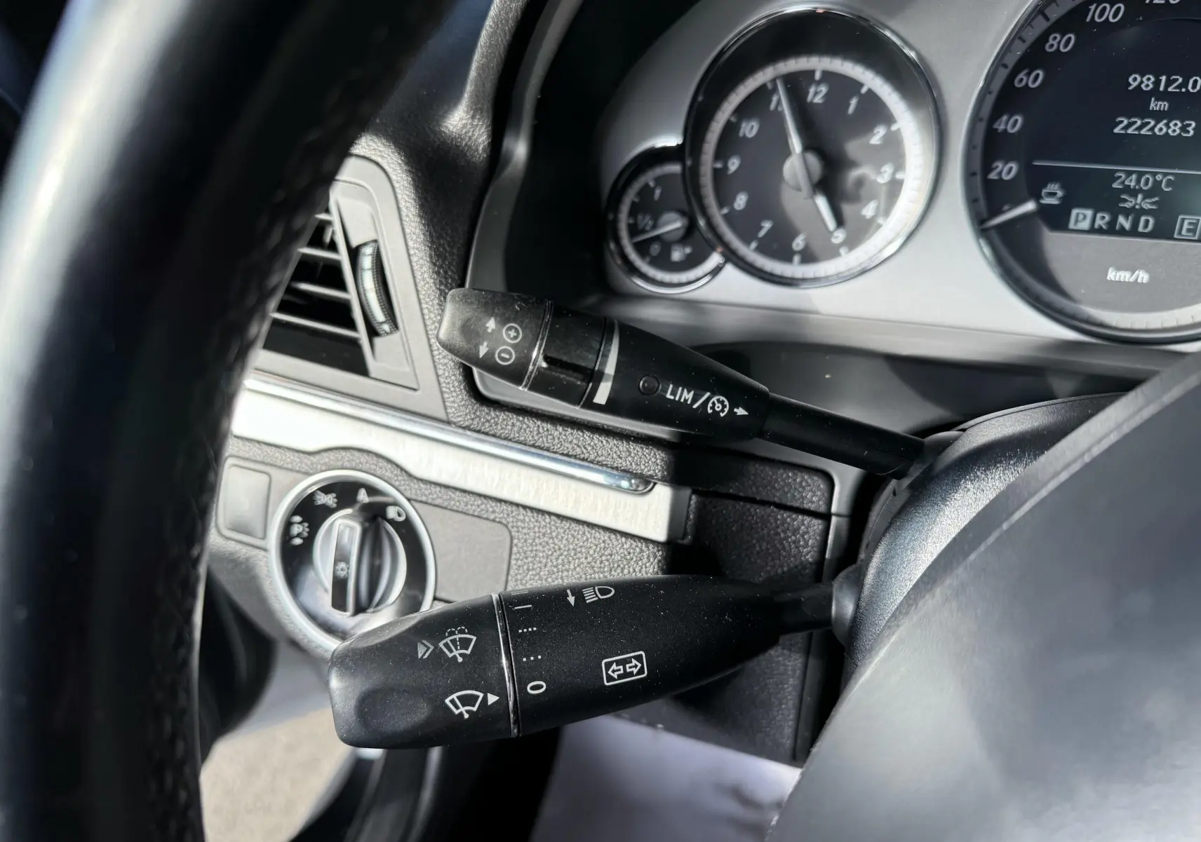 Gros plan sur le tableau de bord et les commandes au volant d'une Mercedes Classe E 250 Coupé gris, affichant le compteur.