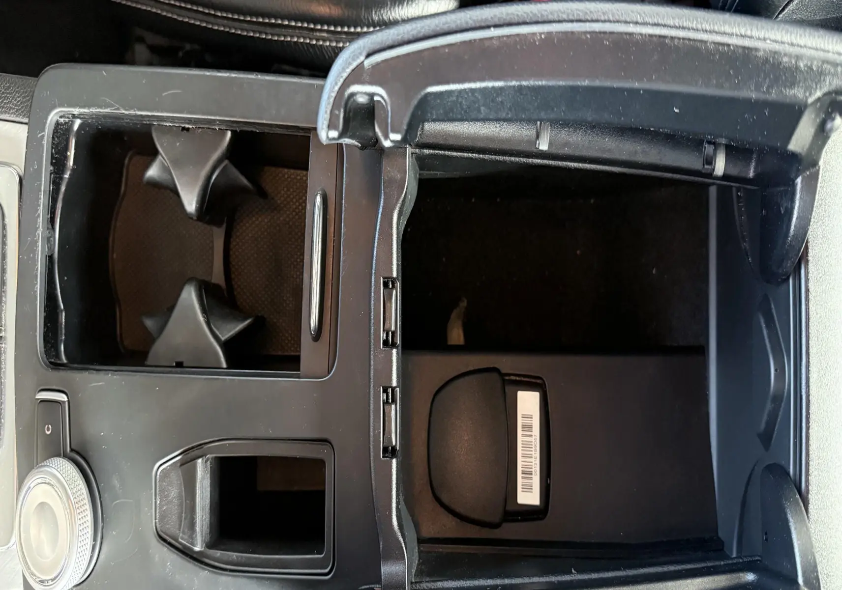 Vue rapprochée de la console centrale ouverte avec porte-gobelets et compartiment de rangement, sièges en cuir noir visibles.