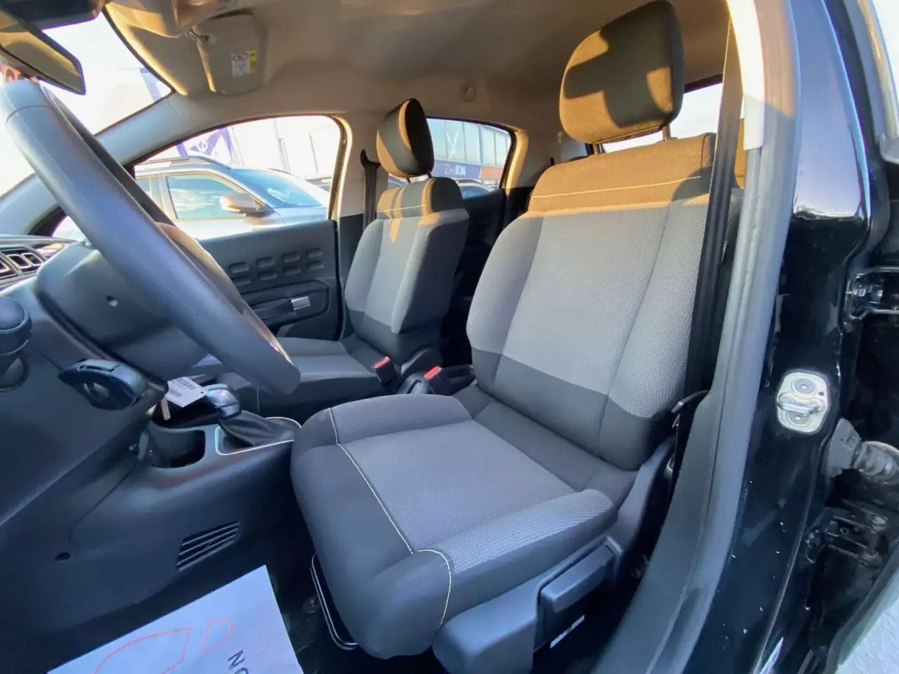 Vue intérieure côté conducteur de la Citroën C3 Shine 2023 avec sièges tissu gris et noir, portière ouverte noir toit rouge.