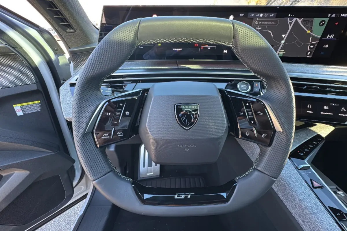 Vue rapprochée du volant cuir perforé noir avec logo Peugeot et inscription GT du 3008 Hybrid blanc okénite 2024.