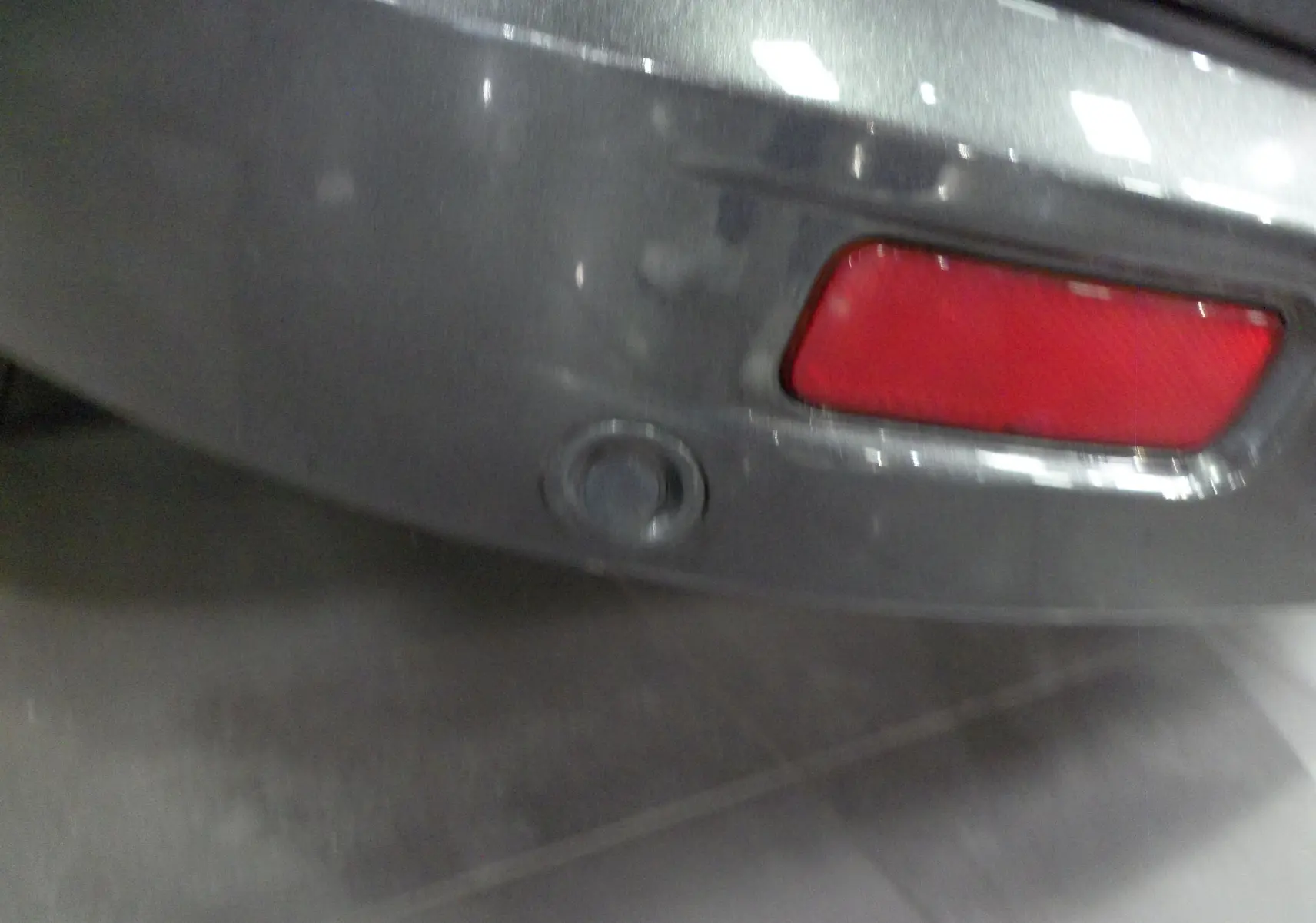 Gros plan sur le capteur de recul et le feu arrière rouge du pare-chocs gris Magnetic d'un Ford Grand Tourneo Connect 2020.