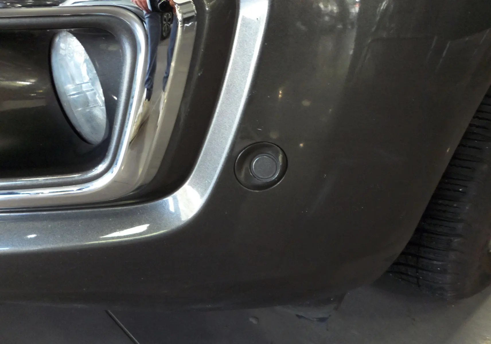 Gros plan sur le pare-chocs avant gris Magnetic du Ford Grand Tourneo Connect 2020 avec capteur de stationnement visible.