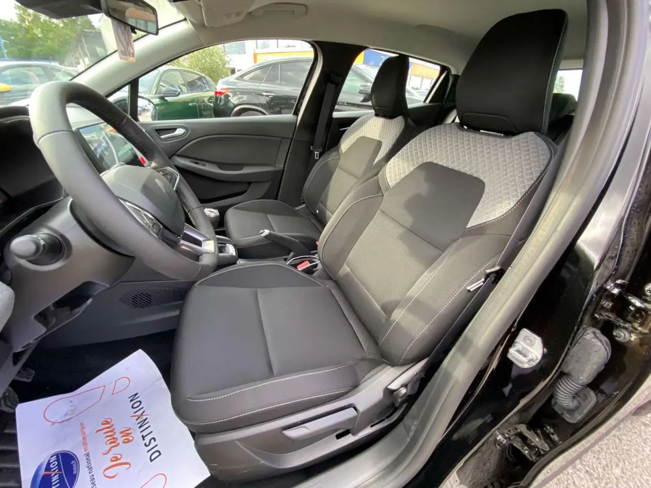 Vue intérieure côté conducteur de la Renault Clio 2025 noir étoilé avec sièges tissu bicolore et volant multifonction.