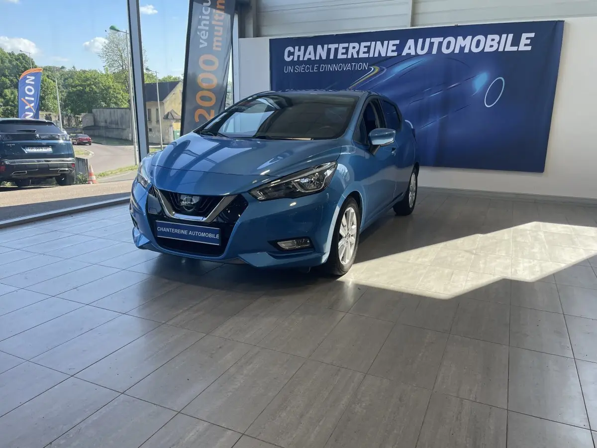 Nissan Micra bleu en 3/4 avant droit dans un showroom avec bannière Chantereine Automobile en arrière-plan.