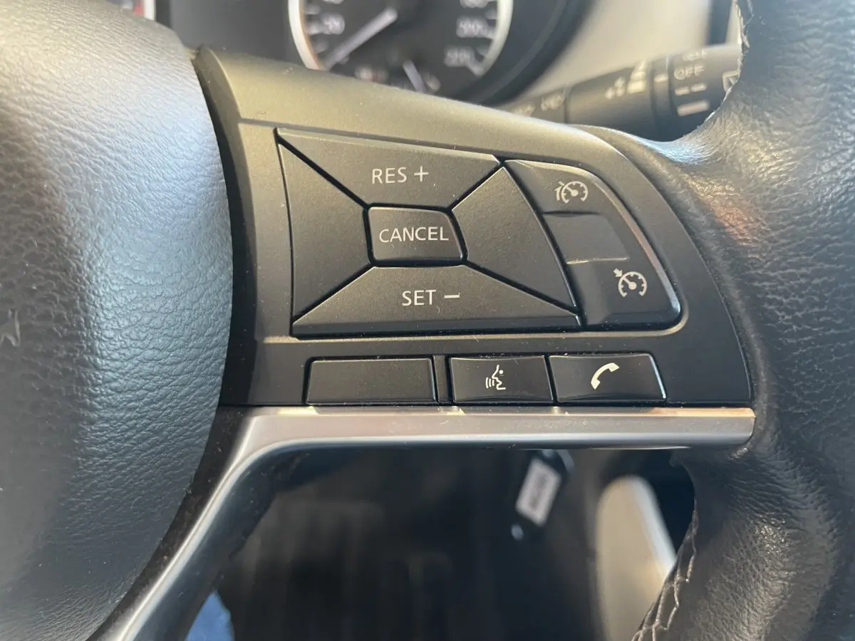 Gros plan sur les commandes de régulateur de vitesse et téléphone au volant cuir noir de la Nissan Micra bleu 2020.