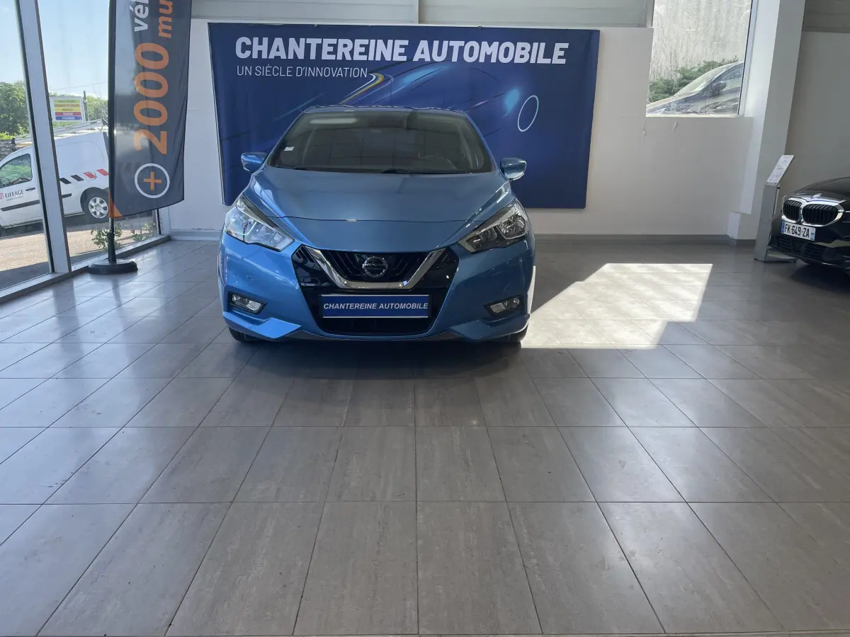 Vue de face d'une Nissan Micra IG-T 100 N-Connecta bleue exposée en showroom avec logo Nissan visible sur la calandre.