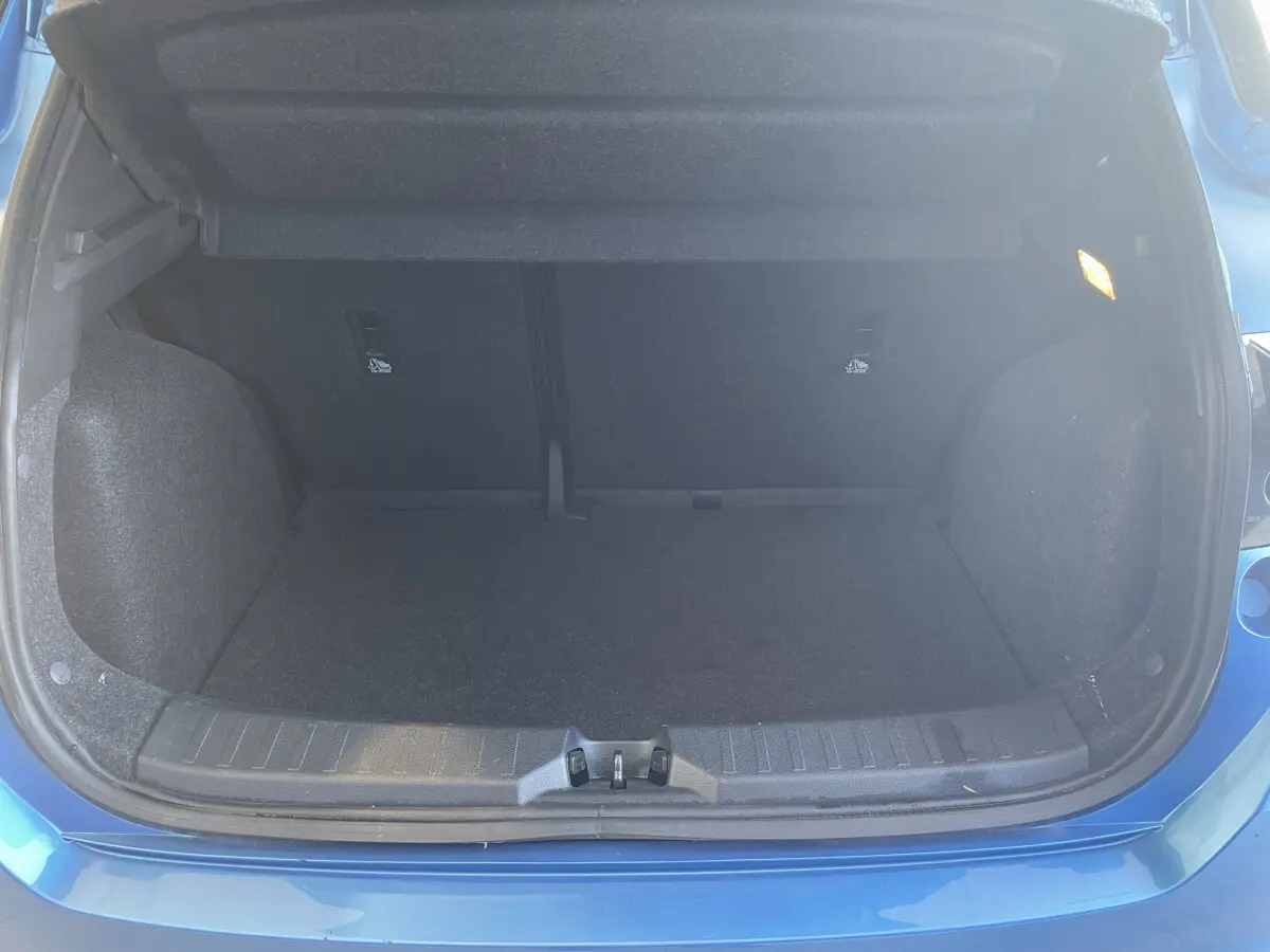 Coffre ouvert vu de l'arrière d'une Nissan Micra IG-T 100 N-Connecta bleu, espace de chargement vide et éclairage intérieur allumé.