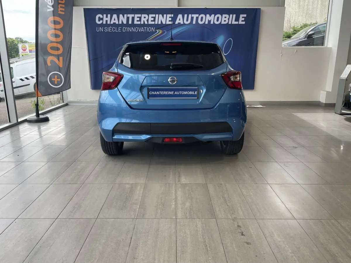 Vue arrière d'une Nissan Micra bleu vif en showroom, avec logo et feux arrière distinctifs bien visibles.