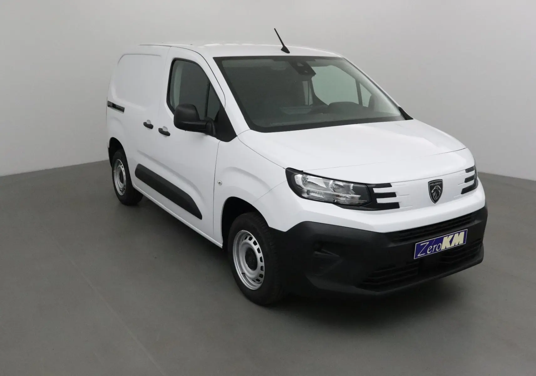 Peugeot Partner blanc vu en 3/4 avant droit, avec pare-chocs noir et logo lion distinctif sur la calandre.