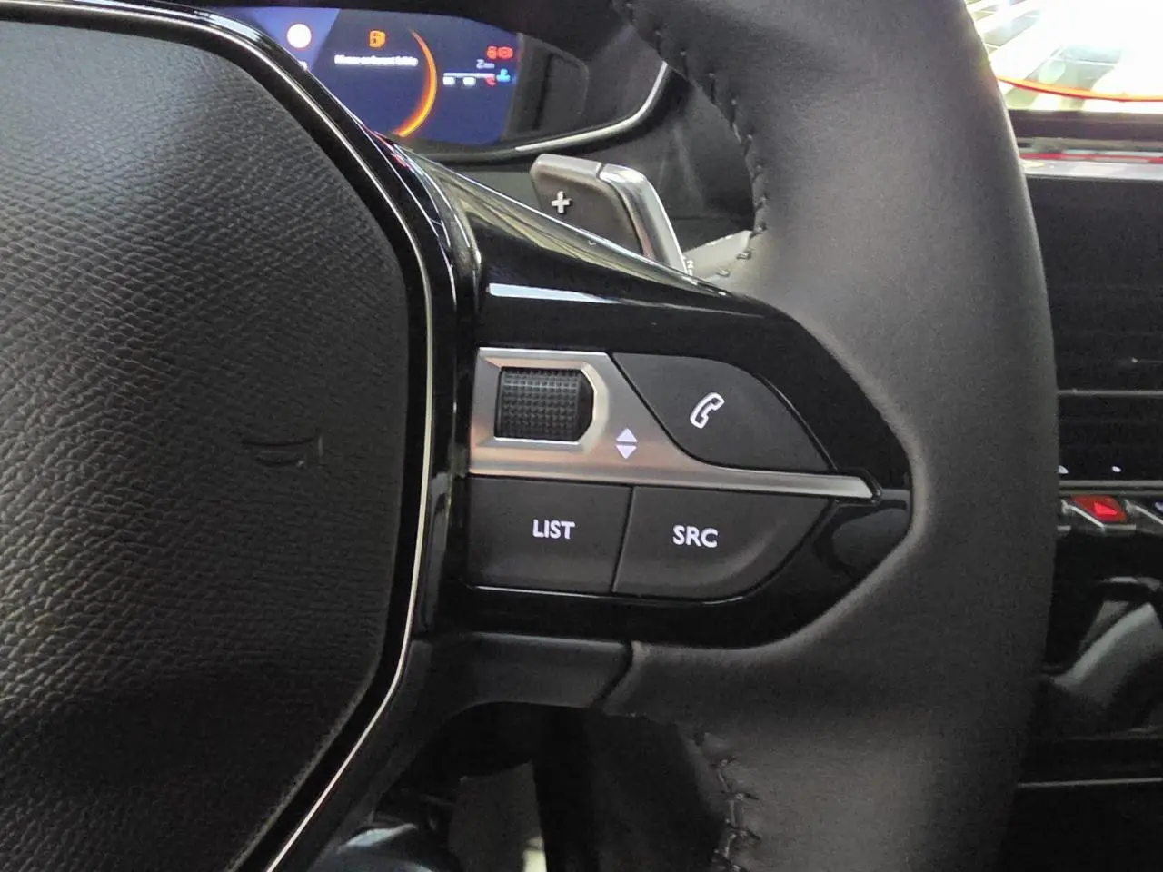 Gros plan sur la partie gauche du volant noir du Peugeot 208 1.2i Hybrid avec commandes multimédia intégrées.