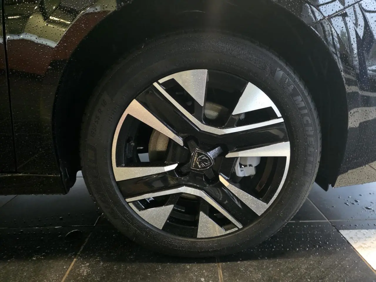 Gros plan sur la jante alliage 16'' bi-tons noir et argentée de la Peugeot 208 noire métallisée, roue avant droite.