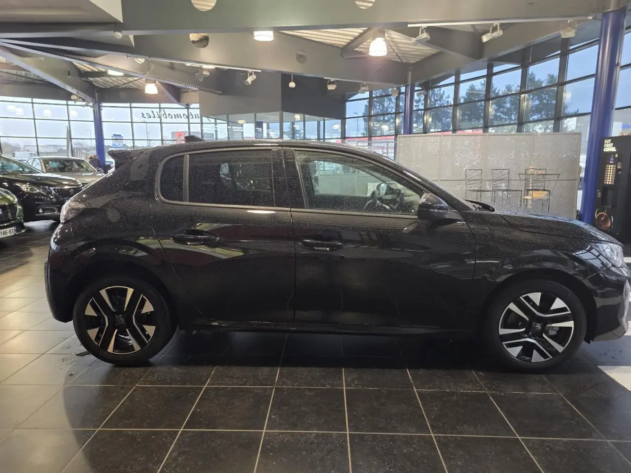 Peugeot 208 noire métallisée vue de profil côté gauche, avec jantes alliage bi-tons et vitres teintées.