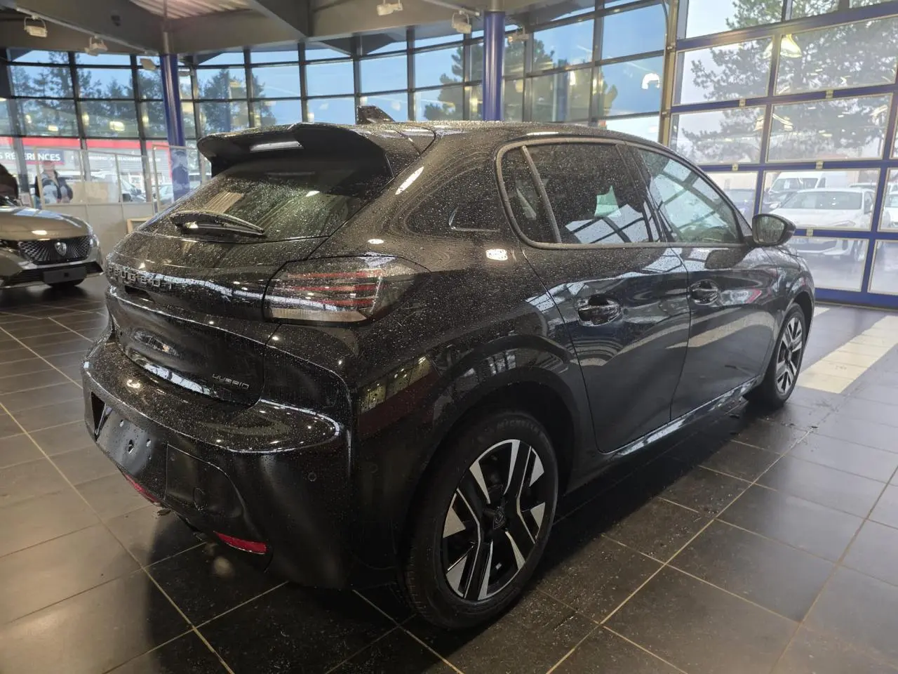 Peugeot 208 hybride noir métallisé vue 3/4 arrière droit en intérieur avec jantes alliage bicolores.