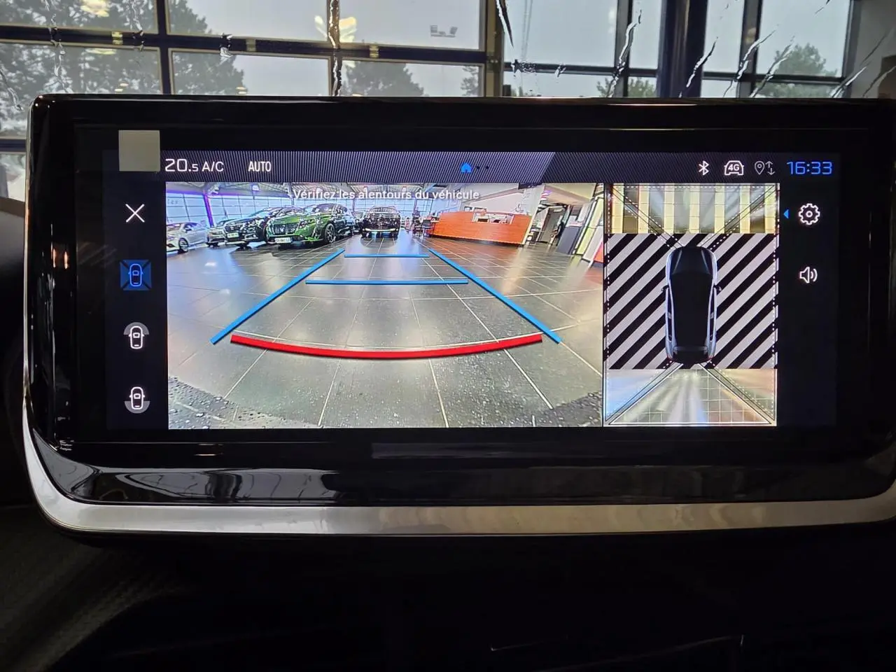 Écran tactile affichant la caméra de recul et vue 360° d’une Peugeot 208 noire métallisée en stationnement intérieur.