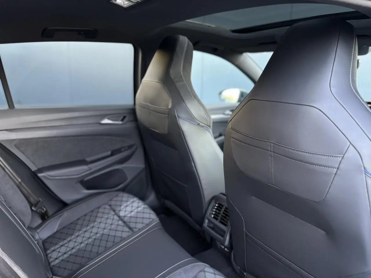 Vue intérieure arrière droite de la Volkswagen Golf VIII R-Line 2026, sièges sport en cuir noir avec surpiqûres bleues.