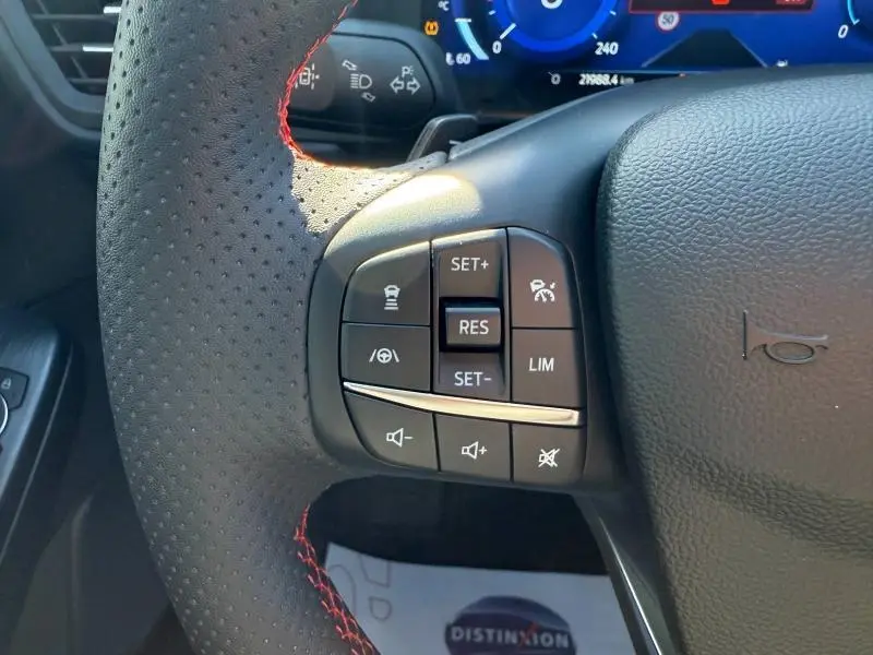 Gros plan sur le volant cuir noir perforé avec surpiqûres rouges du Ford Kuga 2024, boutons de commande multifonction visibles.