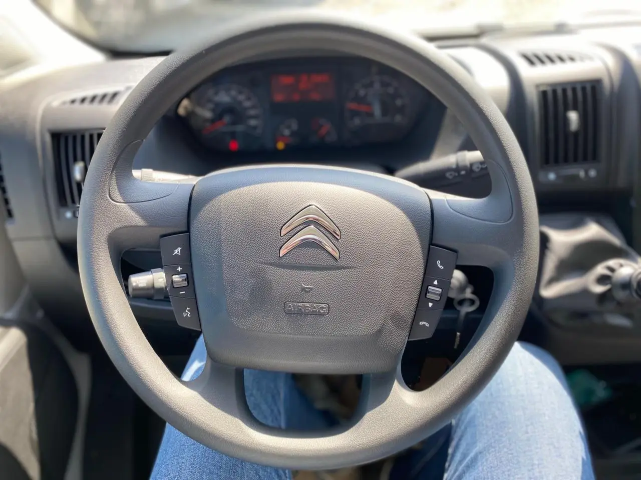 Vue rapprochée du volant noir du Citroën Jumper 2023 avec commandes intégrées et tableau de bord en arrière-plan.