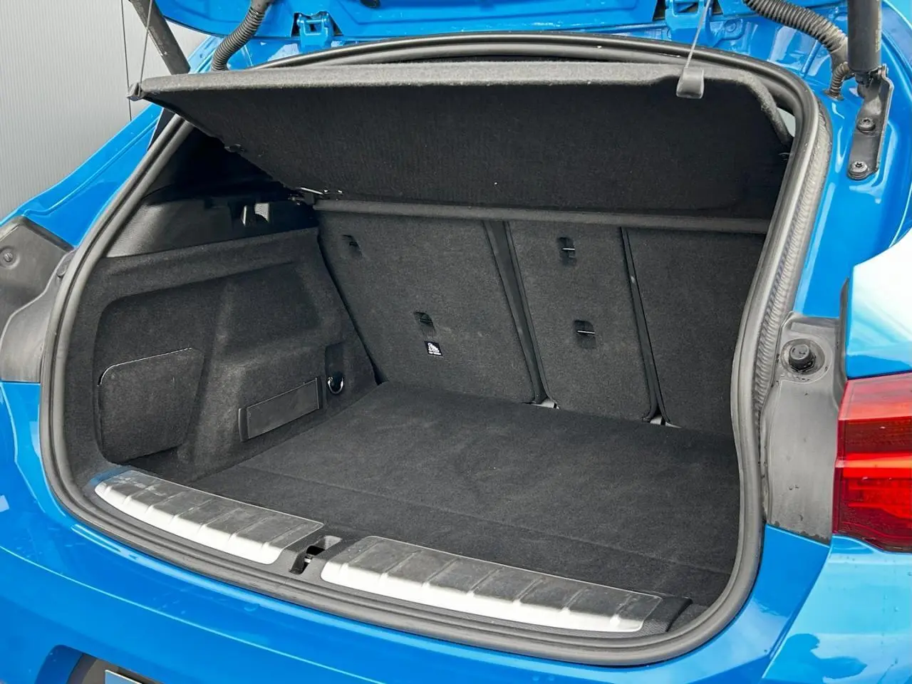 Coffre ouvert vu de l'arrière d'une BMW X2 F39 xDrive 25e bleu Misano avec hayon électrique et tapis noir.
