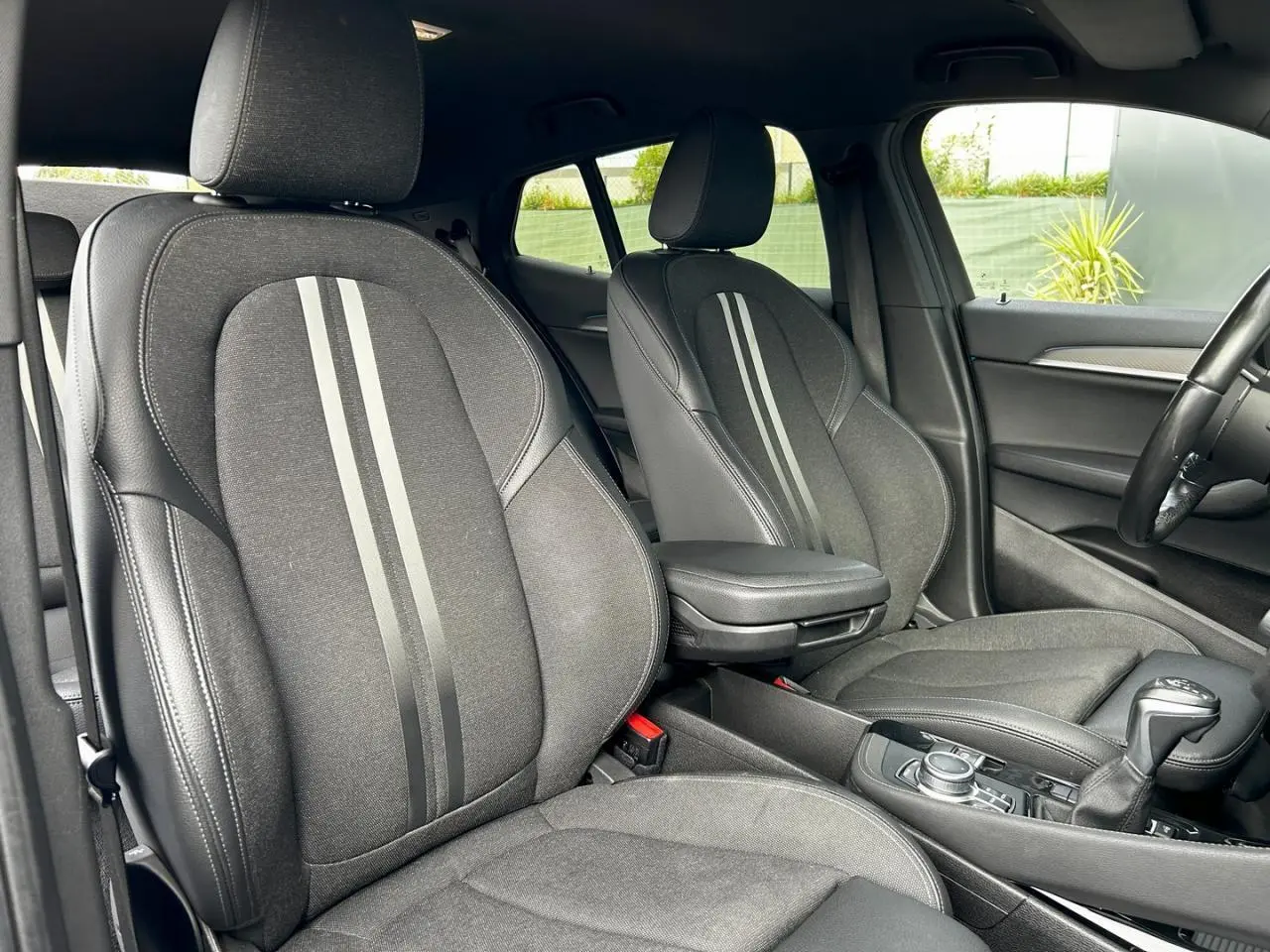 Vue intérieure de profil droit des sièges avant noirs avec bandes grises et accoudoir central dans une BMW X2 F39 2021.
