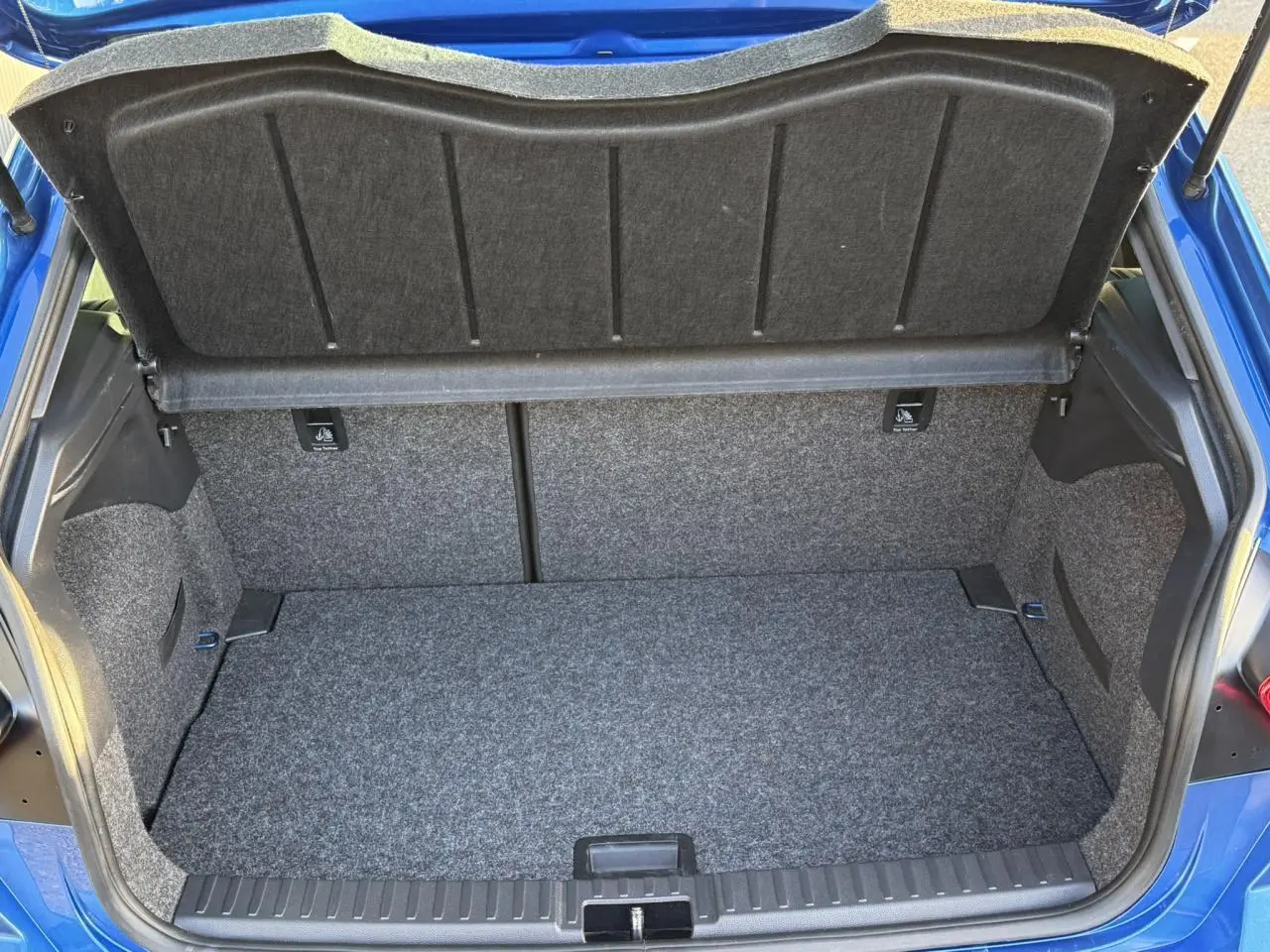 Coffre ouvert vu de l'arrière d'une SEAT IBIZA bleu saphir, montrant l'espace de chargement tapissé gris.