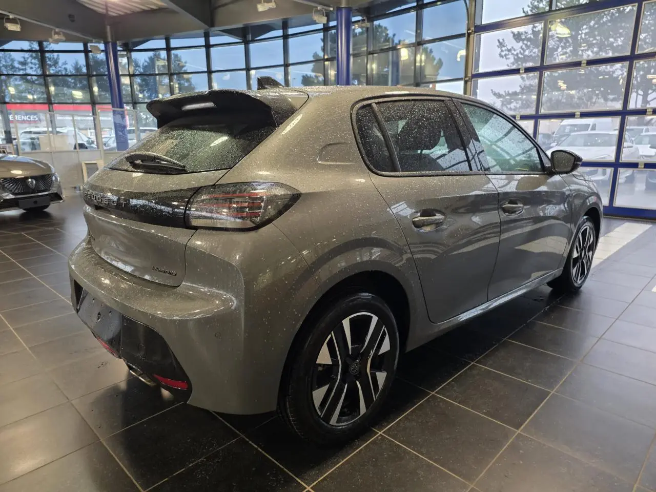 Peugeot 208 gris Selenium vue 3/4 arrière droit en intérieur, avec jantes alliage bi-tons et becquet noir brillant.