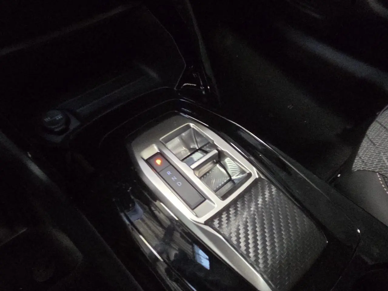 Gros plan sur la console centrale de la Peugeot 208 hybride 2025 avec levier de vitesses automatique et finition carbone.