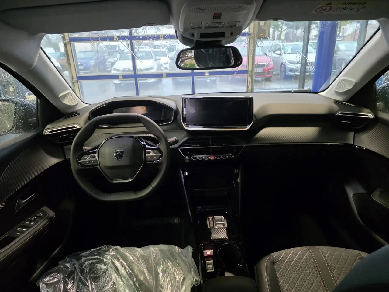 Vue intérieure avant du Peugeot 208 2025 avec tableau de bord noir, volant compact et écran tactile central.