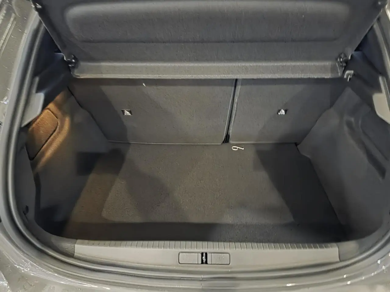 Coffre ouvert de Peugeot 208 gris Selenium, montrant l'espace de chargement vide et la moquette noire.