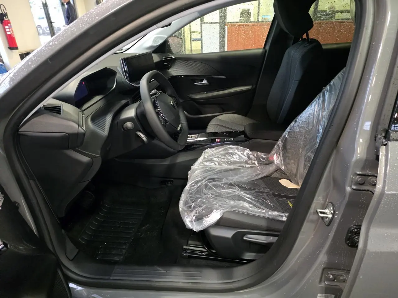 Vue intérieure côté conducteur de la Peugeot 208 gris selenium, montrant le tableau de bord et siège avant protégé.