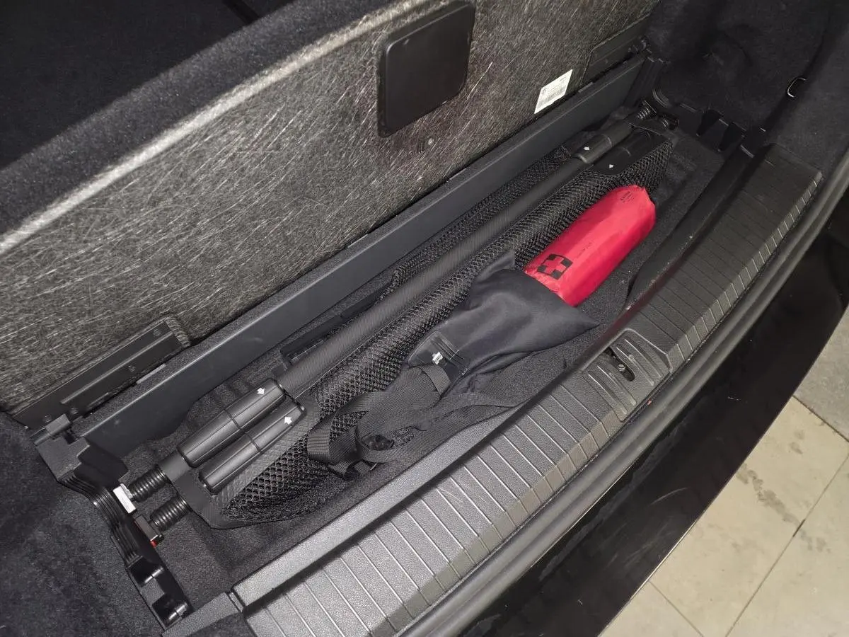 Vue en plongée sur le coffre noir du Volkswagen Touran 2025, montrant le rangement sous plancher avec accessoires.