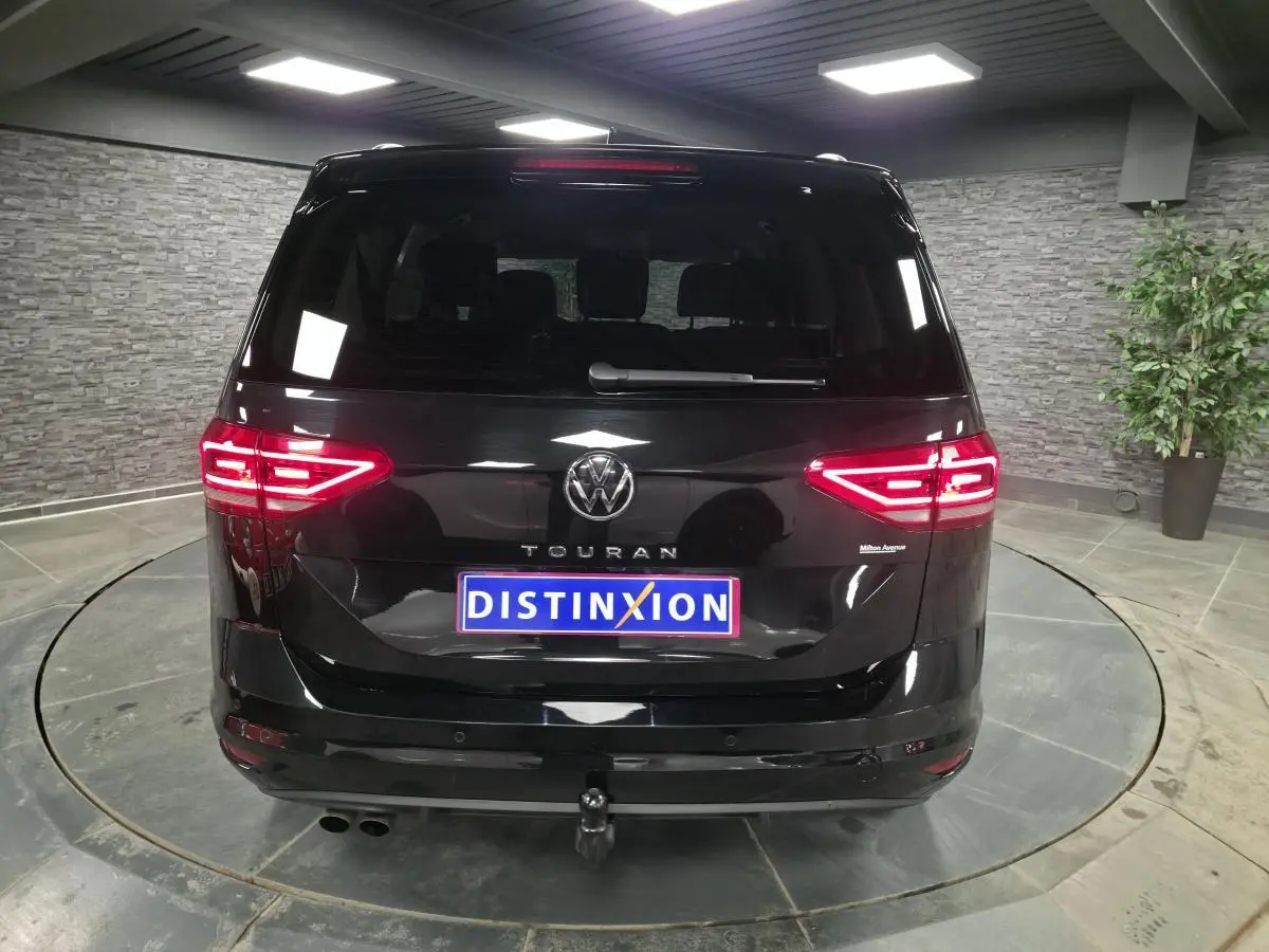 Vue arrière d'un Volkswagen Touran noir 2025 avec feux allumés et crochet d'attelage électrique visible.