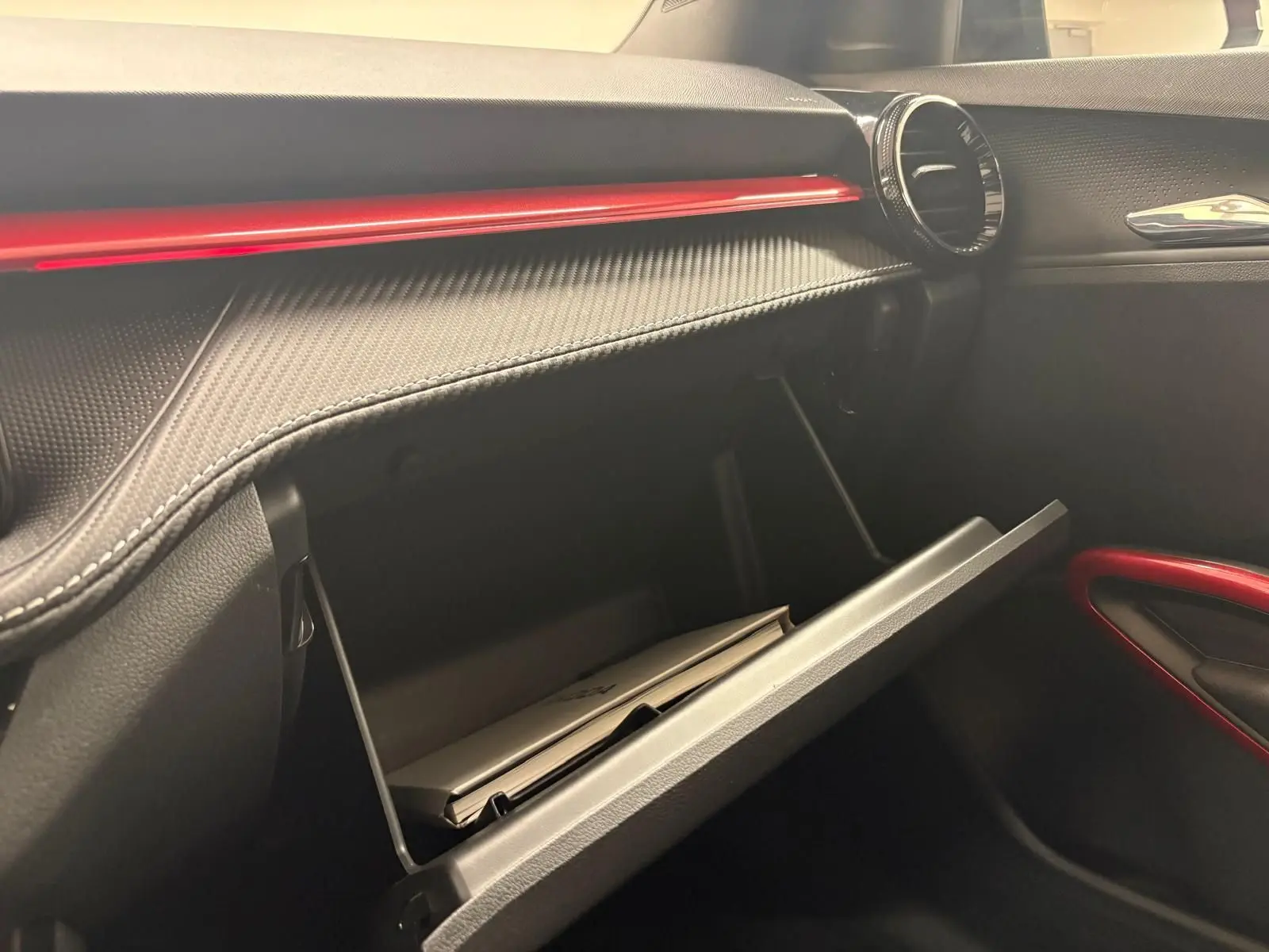 Vue intérieure côté passager du tableau de bord noir avec insert rouge et boîte à gants ouverte d'une Skoda Fabia Monte Carlo 2025.