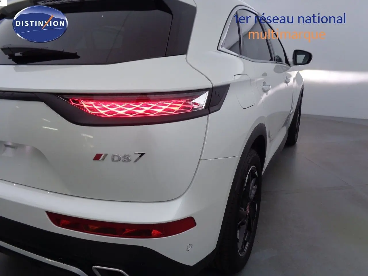 Vue 3/4 arrière droite du DS7 Crossback blanc nacré avec feux arrière LED allumés dans un intérieur lumineux.