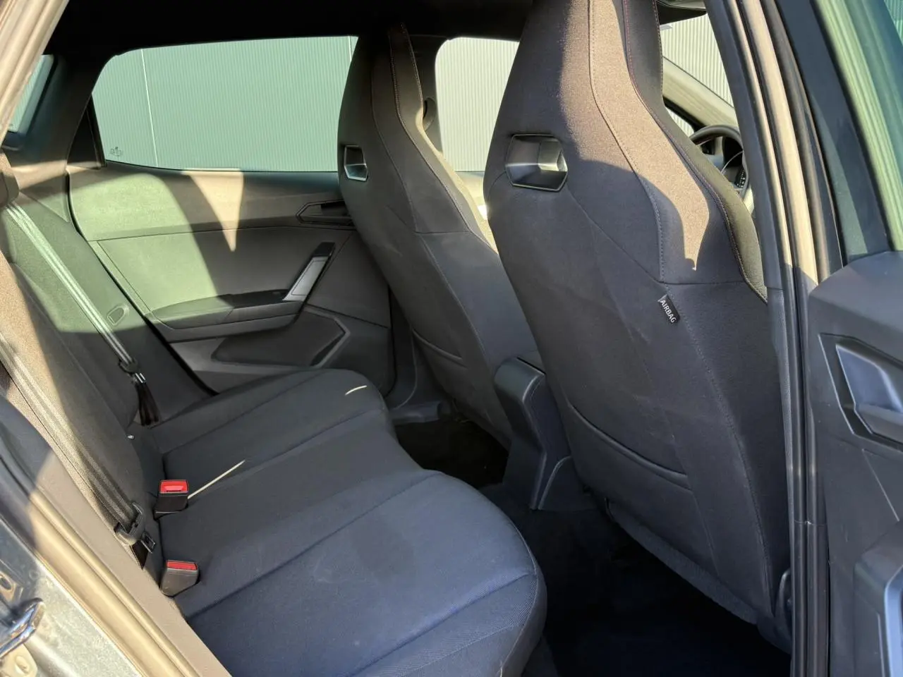 Vue intérieure côté arrière droit de la SEAT IBIZA TSI 115 FR 2025 avec sièges tissu noirs et garnitures sombres.