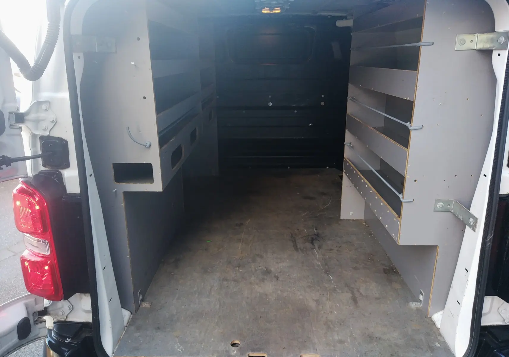 Vue arrière du fourgon blanc Citroën Jumpy 2021, montrant l'intérieur aménagé avec étagères et plancher en bois.