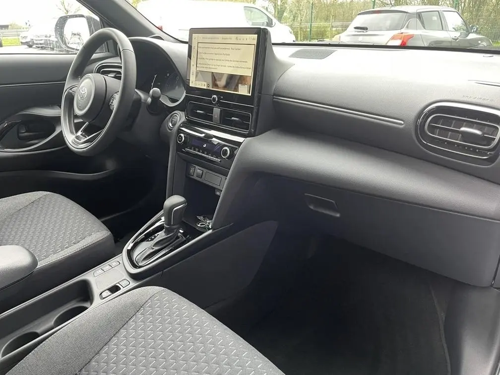 Intérieur avant droit de la Toyota Yaris Cross 2026 gris clair, volant cuir, écran tactile vertical et boîte auto visible.