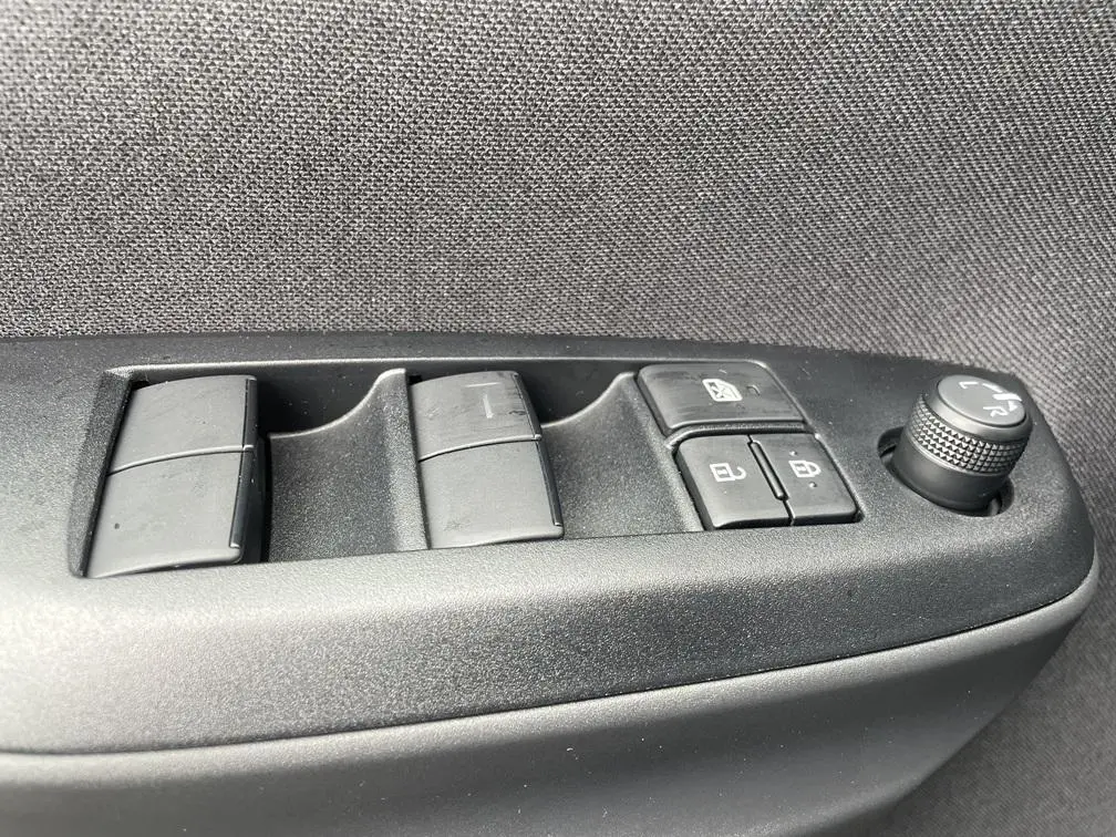 Gros plan sur les commandes de lève-vitres et réglage des rétroviseurs côté gauche d'une Toyota Yaris Cross gris clair.