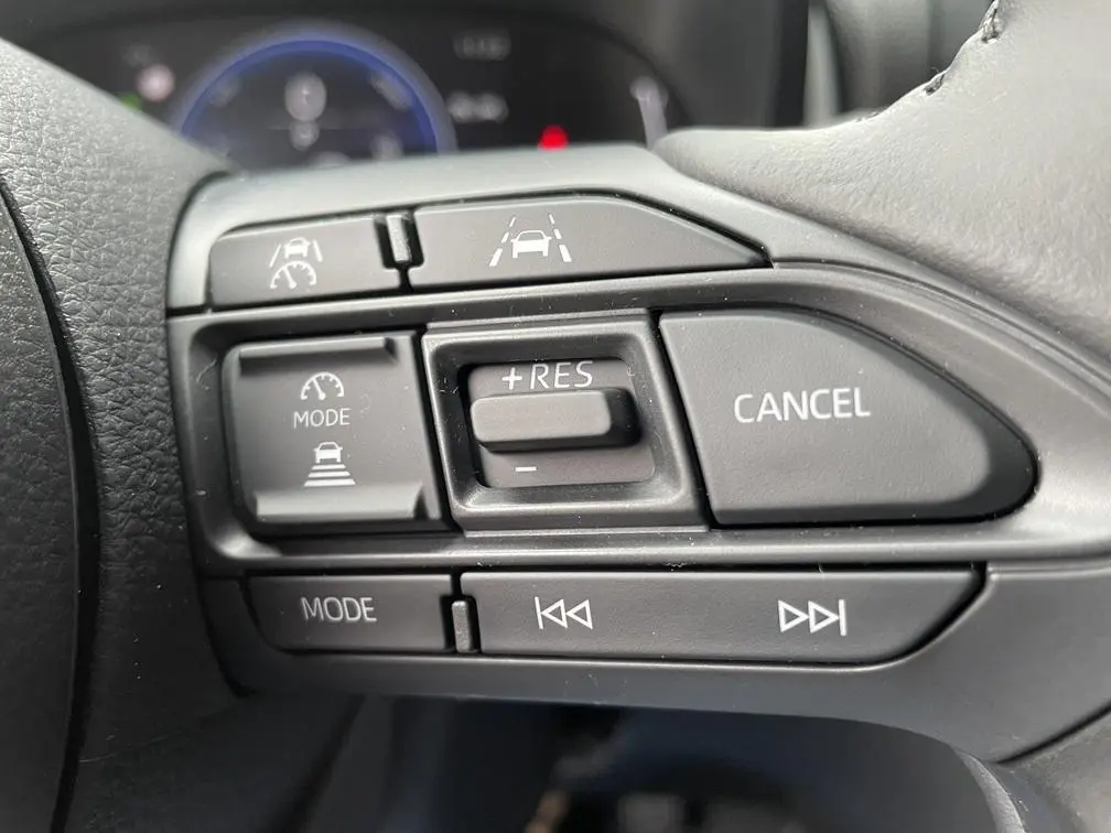 Gros plan sur les commandes multifonctions du volant cuir de la Toyota Yaris Cross gris clair, avec régulateur adaptatif.