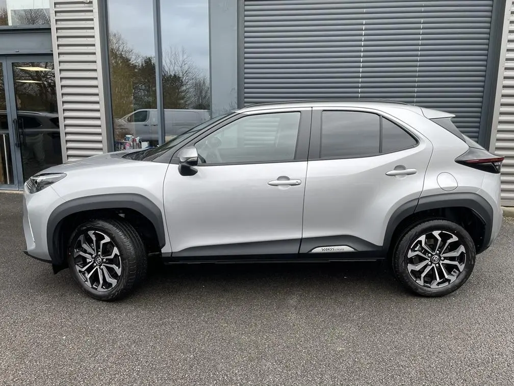 Toyota Yaris Cross gris clair vue de profil côté gauche, avec jantes alliage et protections noires autour des passages de roues.