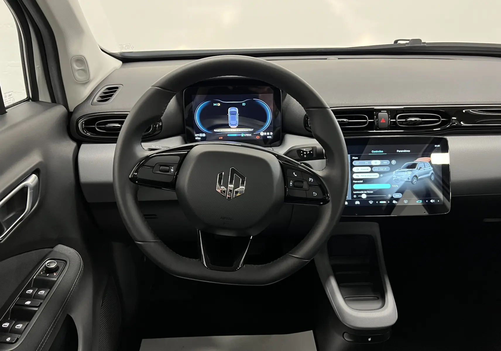 Vue intérieure centrée sur le volant et le tableau de bord numérique de la Dacia Spring blanche électrique avec écran tactile.