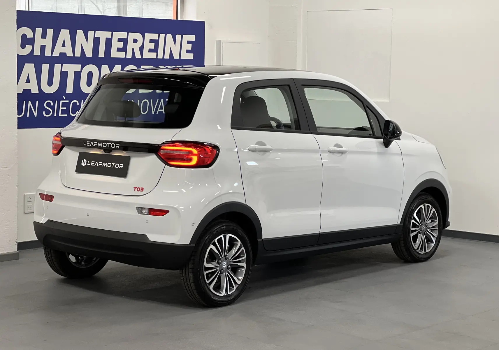 Vue 3/4 arrière droite d'une Dacia Spring blanche électrique LEAP MOTOR T03 avec toit noir et feux arrière allumés.