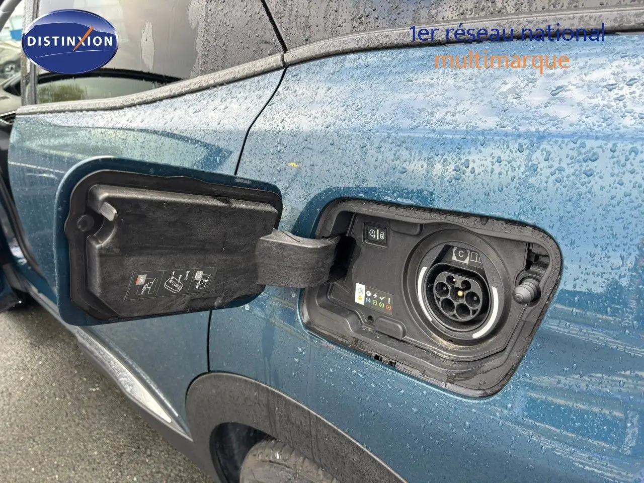 Prise de recharge ouverte côté gauche sur Peugeot 3008 hybride rechargeable bleu Célèbes sous la pluie.
