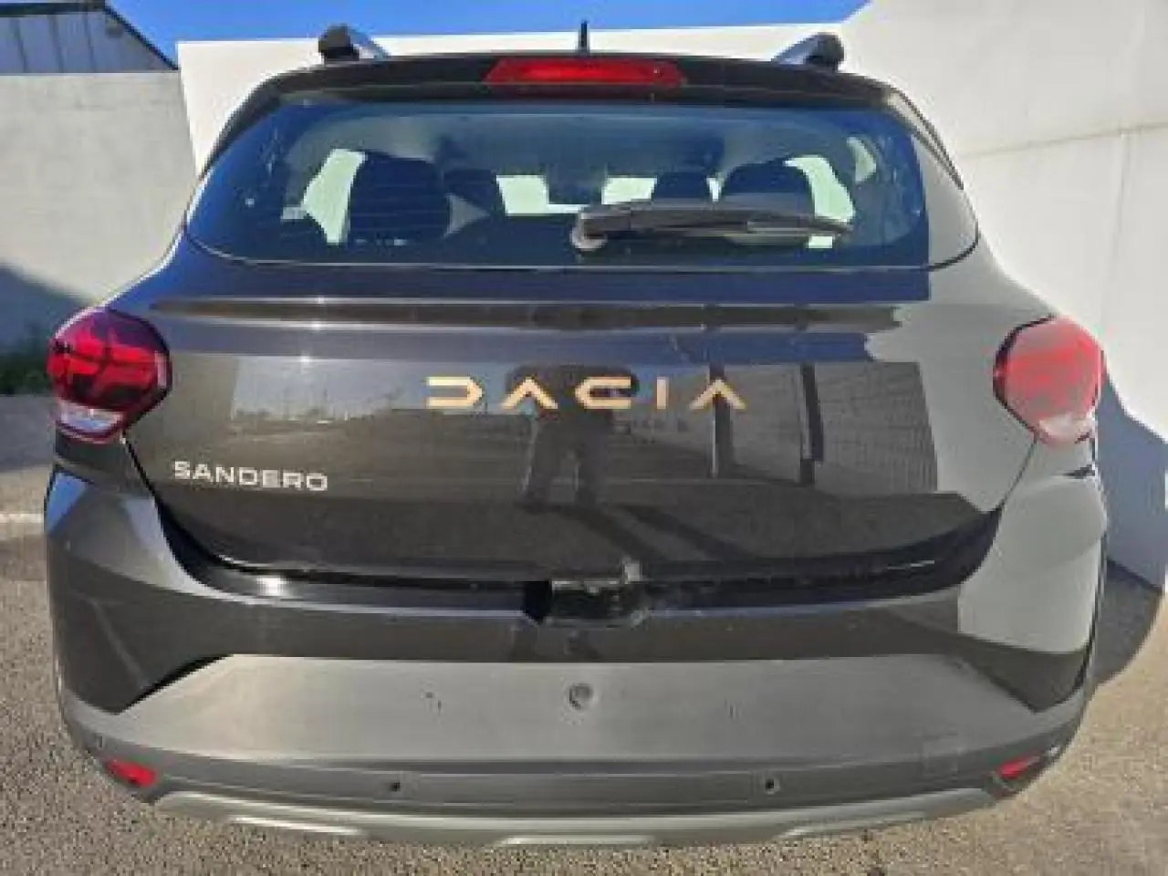 Vue arrière d'une Dacia Sandero III Stepway noire nacrée avec logo doré et feux arrière rouges.