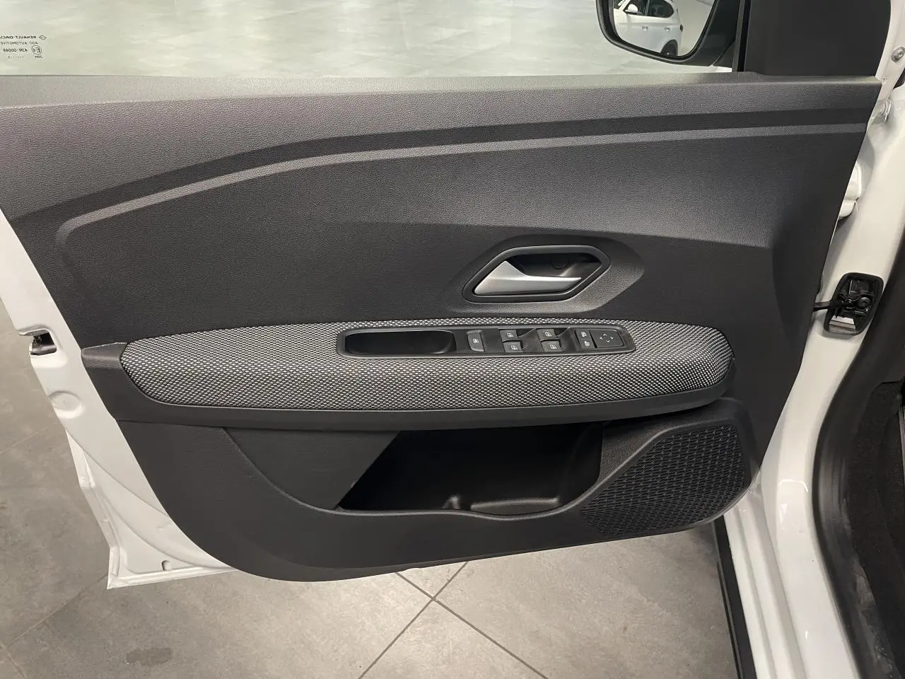 Vue côté intérieur de la porte avant gauche blanche du Dacia Sandero Stepway avec commandes de vitres et poignée grise.